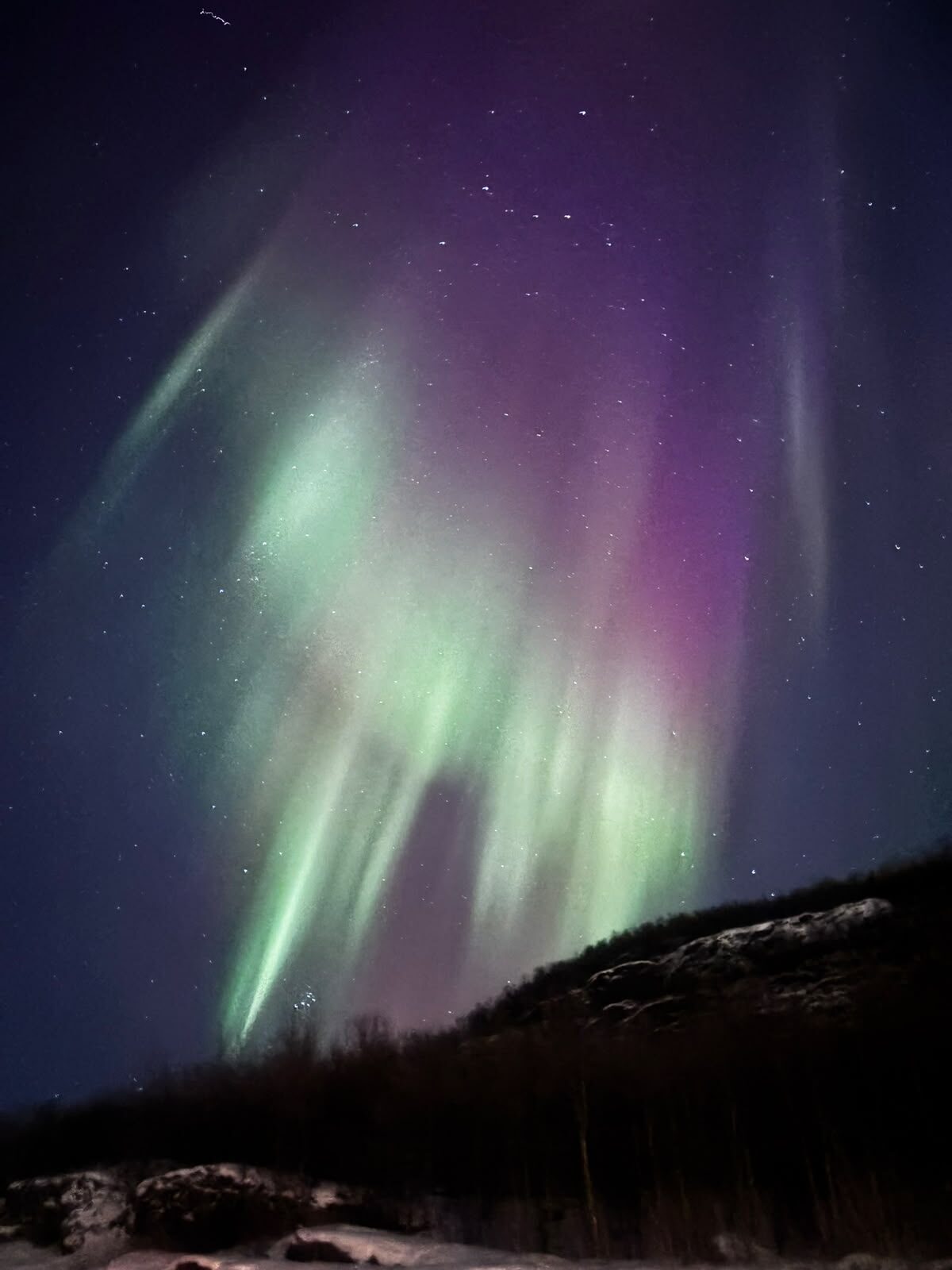 Green and violet aurora above a dark hillside